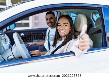 Young hispanic couple smiling happy driving car at the city. Girl doing ok gesture with thumb up.