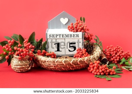 Calendar for September 15 : the name of the month in English, cubes with the number 15 on a decorative tray, branches of red mountain ash around on a crimson background, side view