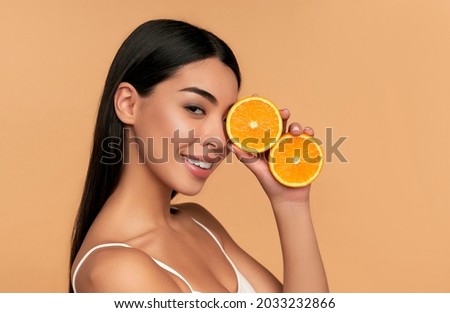 Portrait of Asian girl with shining clean skin of face holding orange halves in white underwear isolated on beige background. Vitamin C cosmetics concept Royalty-Free Stock Photo #2033232866