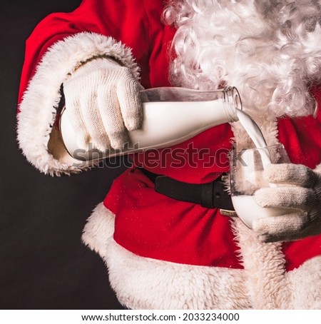 Santa Claus holds a bottle of milk in his hands and pours milk into a glass. Fragment close-up. Royalty-Free Stock Photo #2033234000