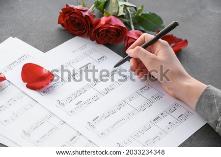 Female hand with pen, roses and music sheets on dark background