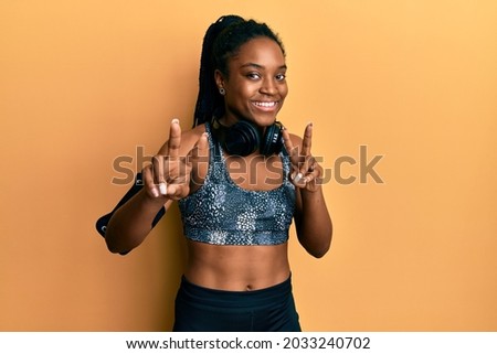 African american woman with braided hair wearing sportswear and arm band smiling looking to the camera showing fingers doing victory sign. number two. 
