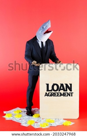 Businessman with a shark head as loan shark holding a wooden board written as Loan Agreement and standing on dollars. Modified generic ball-jointed doll.