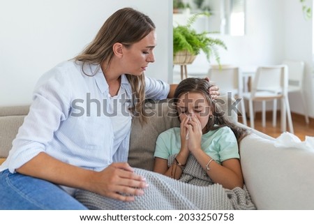 Young woman checking temperature with hand of little ill daughter. Mother checking temperature of her sick girl. Sick child lying on bed under blanket with woman checking fever on forehead by hand.