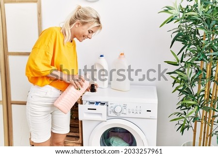 Young blonde girl doing laundry holding detergent bottle at home.