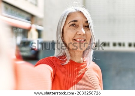 Middle age grey-haired woman smiling happy making selfie by the camera at the city.