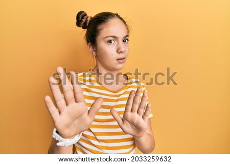 Beautiful brunette little girl wearing casual striped t shirt moving away hands palms showing refusal and denial with afraid and disgusting expression. stop and forbidden. 