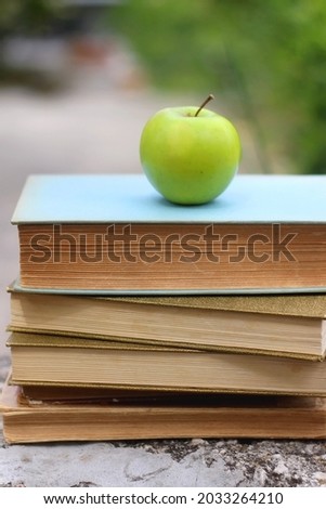 Stack of hardcover books and green apple in a garden. Selective focus. Back to school concept.