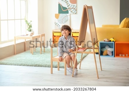 Cute little boy near easel in kindergarten