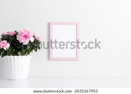 Pink frame mockup on white wall with pink flowers in pot decoration. Front view