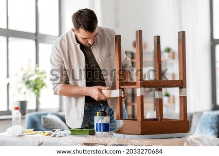 repair, diy and home improvement concept - man sticking adhesive tape to old wooden table for repainting it Royalty-Free Stock Photo #2033270684