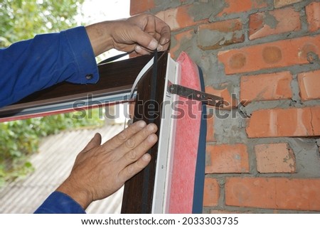 Upvc window installation. A man is installing a self adhesive rubber window seal strip, foam tape, or weather strip to a window frame to windproof and soundproof the window.  Royalty-Free Stock Photo #2033303735