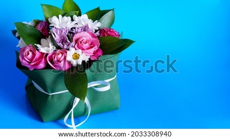 bright juicy bouquet of different colors of pink roses, white daisies and purple peonies in green leaves, collected in one green box on a blue background. Bright floral banner.flowers for the holiday