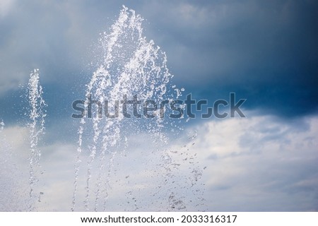 Splashes of a dancing fountain in a summer park against the backdrop of a stormy blue sky. Water jets outdoors in hot weather. 