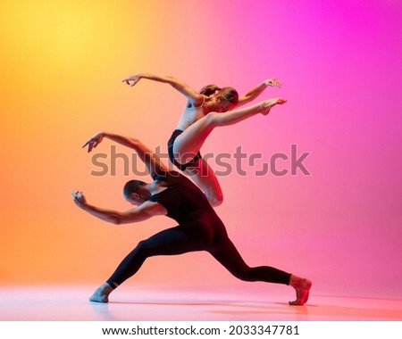 Two dancers, stylish sportive couple dancing contemporary dance on colorful gradient yellow pink background in neon light. Concept of art, creativity, movement, style and fashion, action. Royalty-Free Stock Photo #2033347781