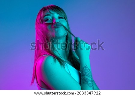 Silly mood, vibe. Portrait of young beautiful girl isolated on blue studio background in neon light filter. Concept of human emotions, facial expression, youth, aspiration, sales. Copy space for ad