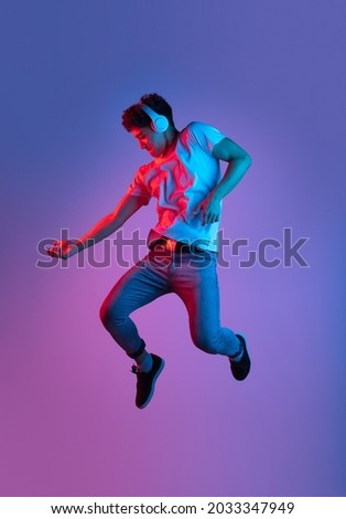 Jumping, flying. Stylish young asian man isolated over lilac color studio background in pink neon light. Concept of human emotions, facial expression, youth culture, diversity. Listening to music