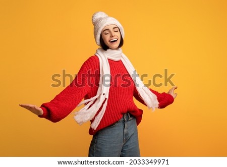 Carefree playful woman in white knitted winter set and red sweater dancing and turning around over yellow studio background, having fun and enjoying winter holidays