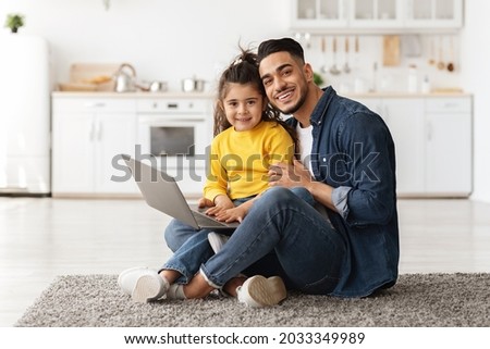 Portrait Of Happy Young Arab Father With Cute Little Daughter Using Laptop Together At Home, Smiling Middle Eastern Family Dad And Female Child Shopping Online Or Browsing Internet On Computer Royalty-Free Stock Photo #2033349989