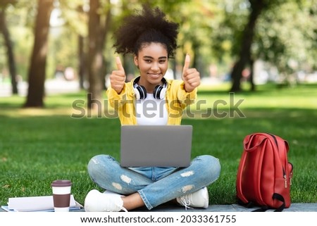Black Student Girl Posing With Laptop Gesturing Thumbs Up Smiling To Camera Learning Sitting Outdoors In Green Park. I Like E-Learning. College Female Approving Distance Online Education Royalty-Free Stock Photo #2033361755