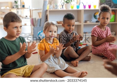 Group of small nursery school children sitting on floor indoors in classroom, clapping. Royalty-Free Stock Photo #2033374145