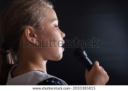 Little talented  girl holding microphone, close up, on black background.