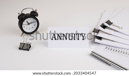 Card with text ANNUITY on a white background, near office supplies and alarm clock. Business