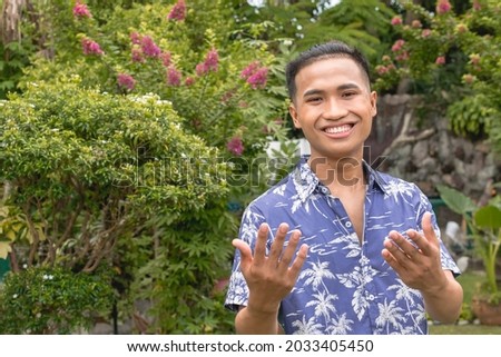 A hospitable young Filipino man welcomes a visitor to a house or resort. Outdoor scene, possible hotel staff. Royalty-Free Stock Photo #2033405450