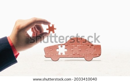 The hand inserts the last piece into the car-shaped puzzle. Car buying, repair, warranty service. Concept. Royalty-Free Stock Photo #2033410040
