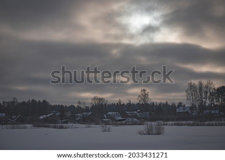 village in Latvia near lake in winter morning, gloomy blurry sunrise, cloudy sky
