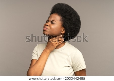 Unhealthy african girl having sore throat, suffering from painful swallowing, strong pain in throat or loss of voice holding neck isolated on studio grey background. Tonsillitis angina thyroid concept Royalty-Free Stock Photo #2033442485