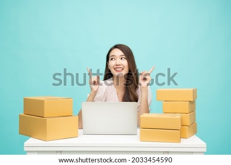Young asian woman startup small business freelance pointing finger up with parcel box and computer laptop on table and sitting isolated on green background, Online marketing and delivery concept Royalty-Free Stock Photo #2033454590