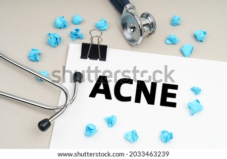 Medicine concept. On the table is a stethoscope, a pen, blue crumpled pieces of paper and a sign with the inscription - ACNE