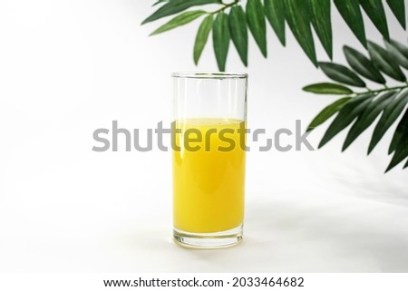 orange juice in a glass on a white background with tropical leaves