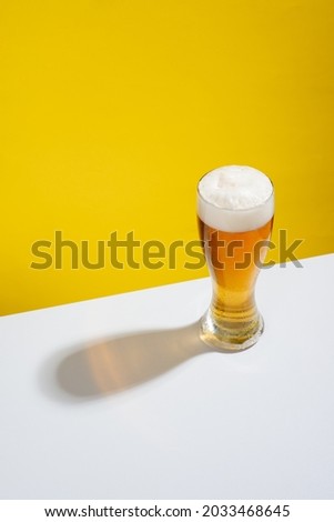 Cold beer served in a glass with white foam on a white table and yellow background, no people Royalty-Free Stock Photo #2033468645