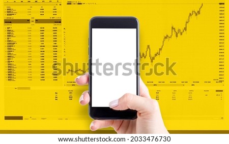Hand holding a phone with a blank screen and stock graphs in the background on a yellow background.