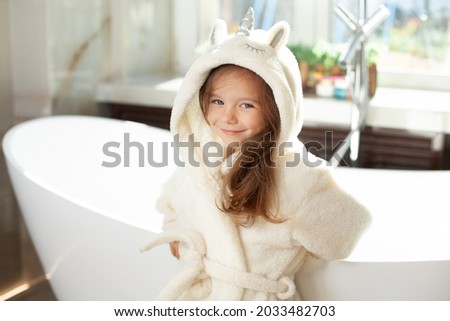 Portrait of a cute girl in a white coat with a unicorn in a bright bathroom with a window. Hygiene. Morning routine. Purity. High quality photo Royalty-Free Stock Photo #2033482703