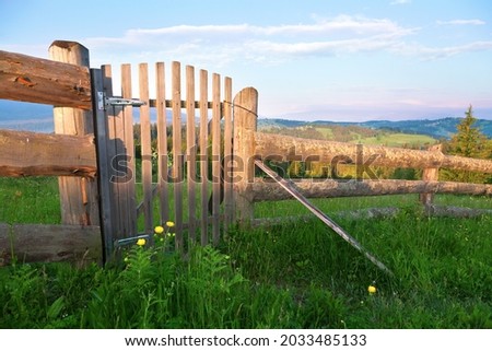 Wooden fence with a gate across a mountain field, lush green grass and flowers. Ukraine, carpathians.
