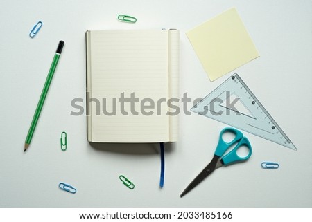 notebook with space for text, desk, reminder, yellow card, blue bookmark, green pencil, ruler, scissors, paper clips, on a white background, photo from above