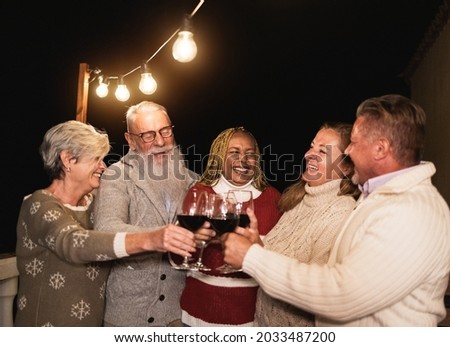 Multiracial senior friends cheering with wine on new years eve - Elderly people celebrating together on patio on christmas time