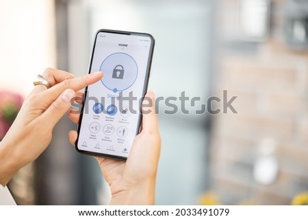 Woman closes the door or turns on the house alarm with a mobile phone. Device with running program for home security. Innovative technologies in home security