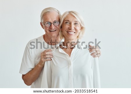 Minimal waist up portrait of modern senior couple embracing against white background and looking at camera