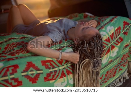 a girl with dreadlocks and a gray dress lies upside down on a bright green blanket in the car. High quality photo