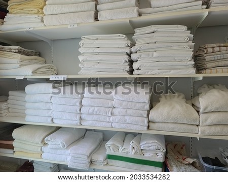 White linens piled neatly on shelves. There are folded bed sheets, towels, wash clothes, and other forms of clothes that are necessary in a hospitality setting. Royalty-Free Stock Photo #2033534282