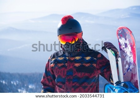 A man in snowboarding gear on the top of a mountain. Young man standing with a snowboard on the top of the mountains