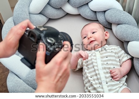 A photographer takes pictures of a newborn baby with a camera on the crib. Photo session of children in the home interior