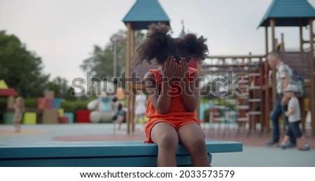 Lonely upset afro-american little girl crying sitting on bench outdoors. Frustrated preschool african kid cry on playground Royalty-Free Stock Photo #2033573579