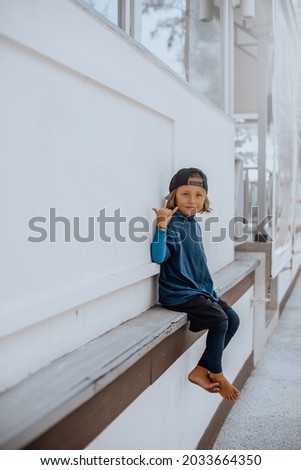 Little kid poses near white wall and shows shaka sign looking at camera