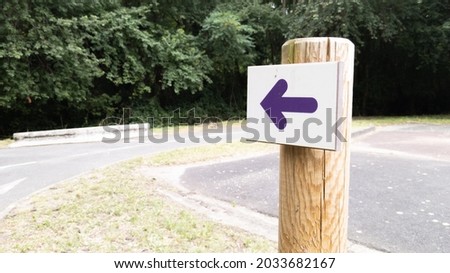 wooden arrow purple pointing the direction of footpath for hike trail escape city path in park