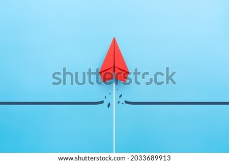 Red paper plane breaking through obstacle on blue background, Concept of overcoming barriers, goal, target Royalty-Free Stock Photo #2033689913
